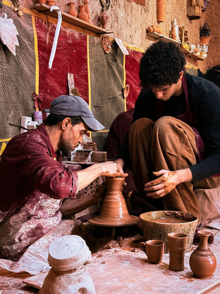 Homme assis qui fait de la poterie et est aidé par un autre homme